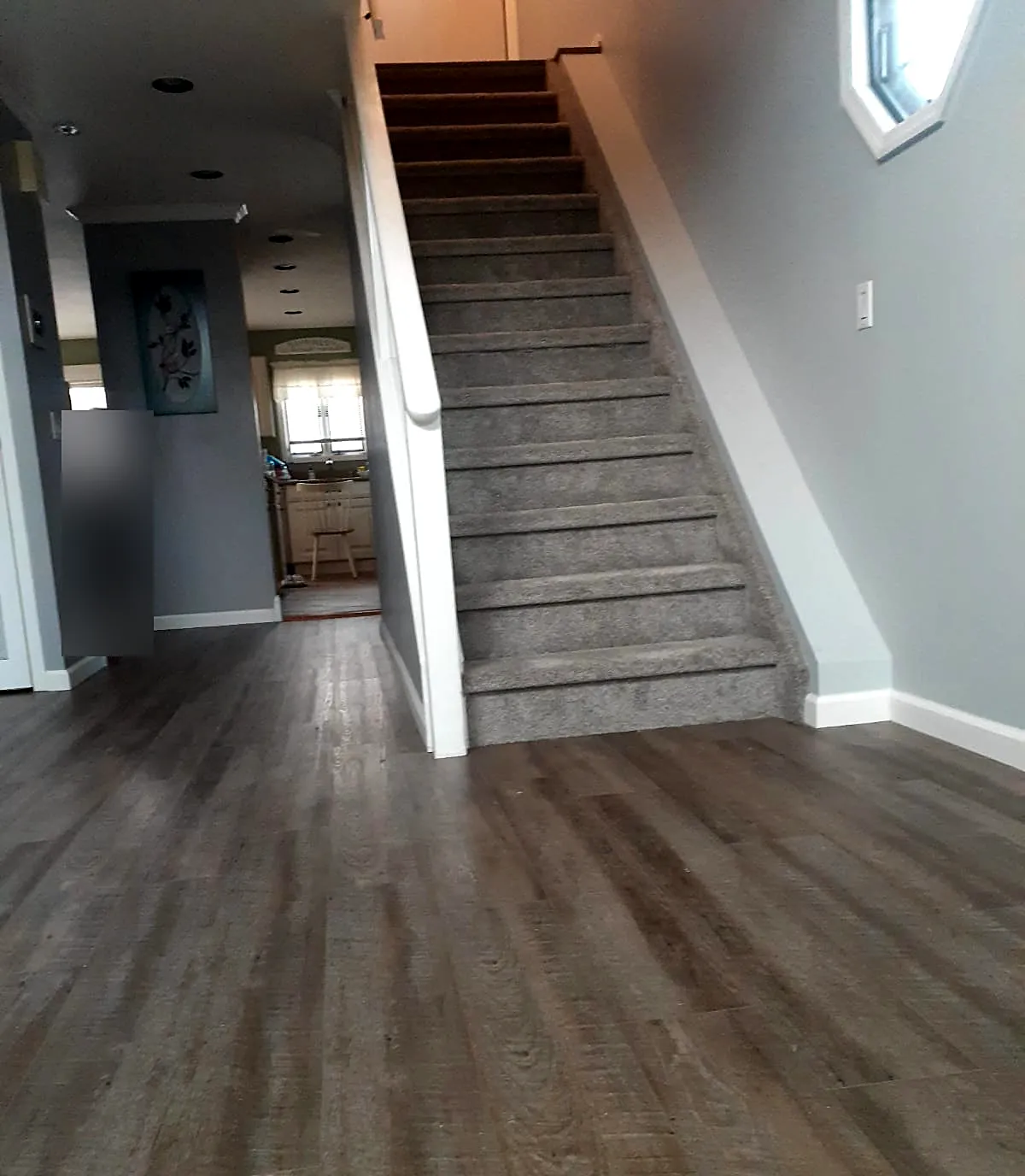 Front hall remodel in Baldwin, NY: a gray wood-look vinyl plank floor at the foot of a gray carpeted staircase