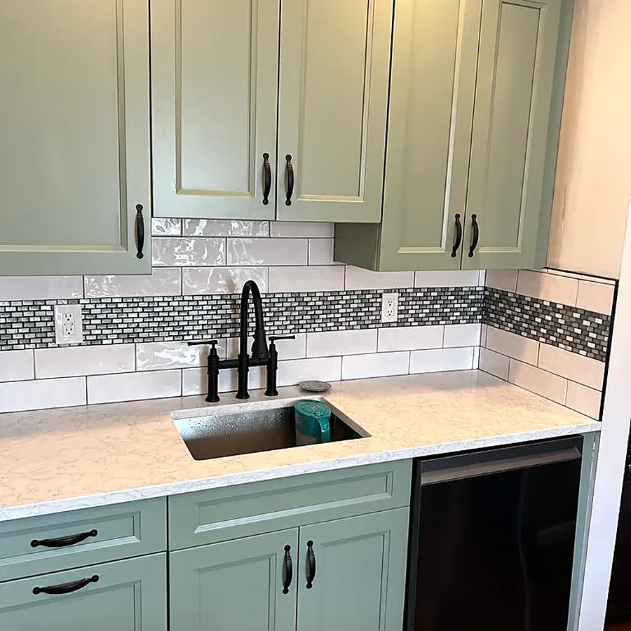 Kitchen remodel in Bethpage, NY: sage green cabinets with black pulls, a white subway backsplash with a mosaic band and a black faucet