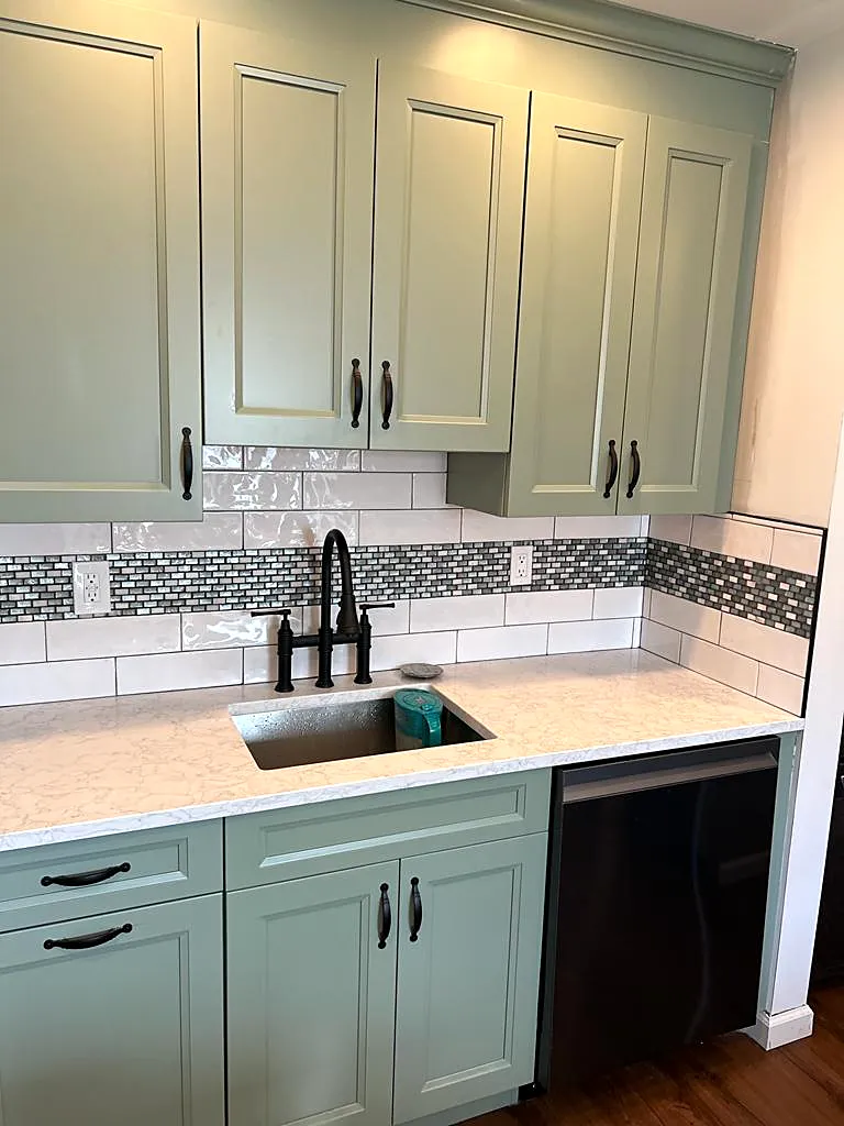 Kitchen remodel in Bethpage, NY: sage green cabinets with black pulls, a white subway backsplash with a mosaic band and a black faucet