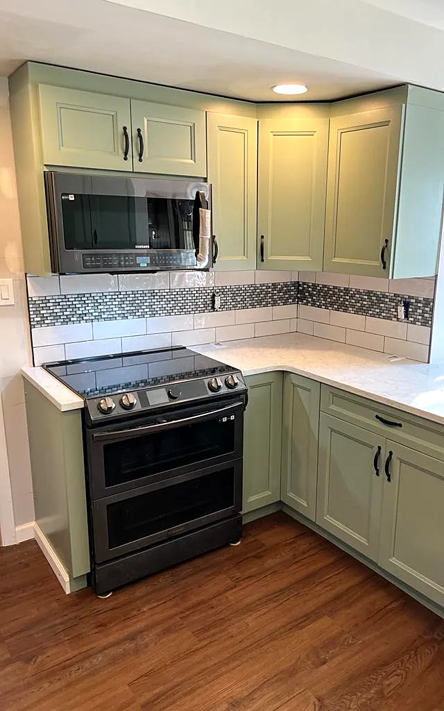 Kitchen remodel in Bethpage, NY: a corner of sage green cabinets with a white stone-look counter, a range and a mosaic tile backsplash band