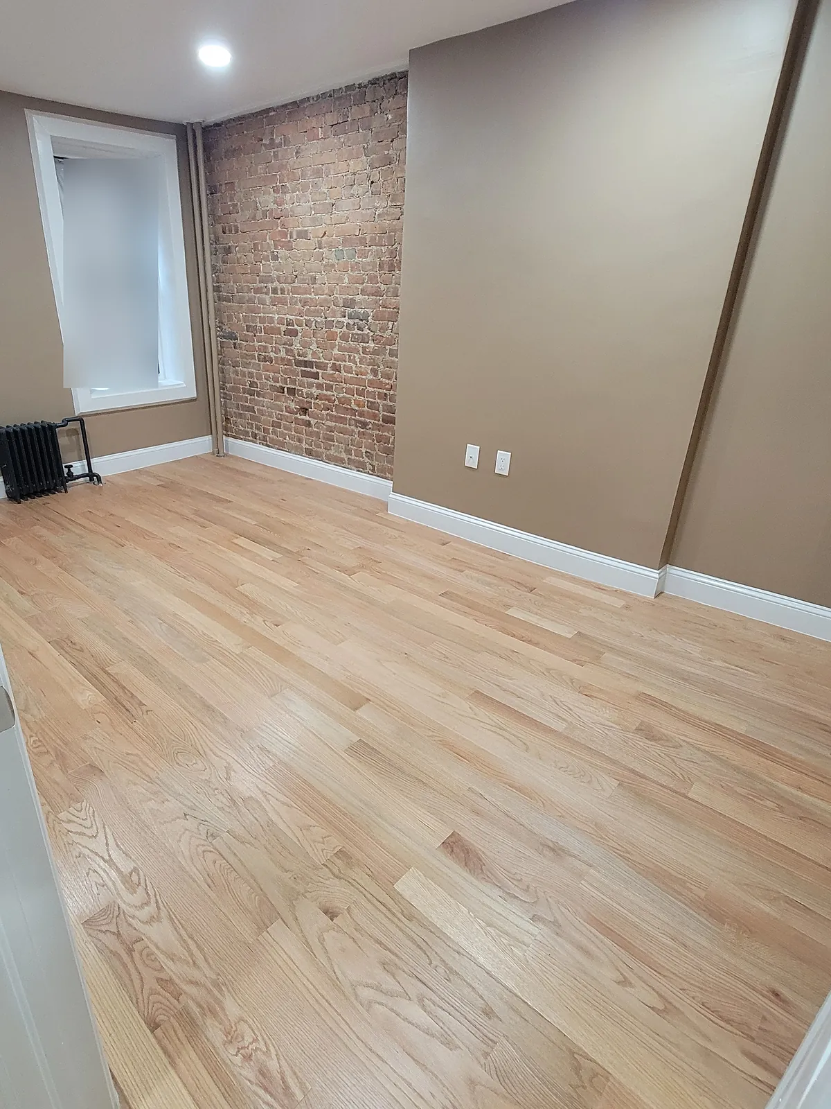 Bedroom remodel in the Bronx, NY: a new light wood plank floor, an exposed brick wall and tan walls