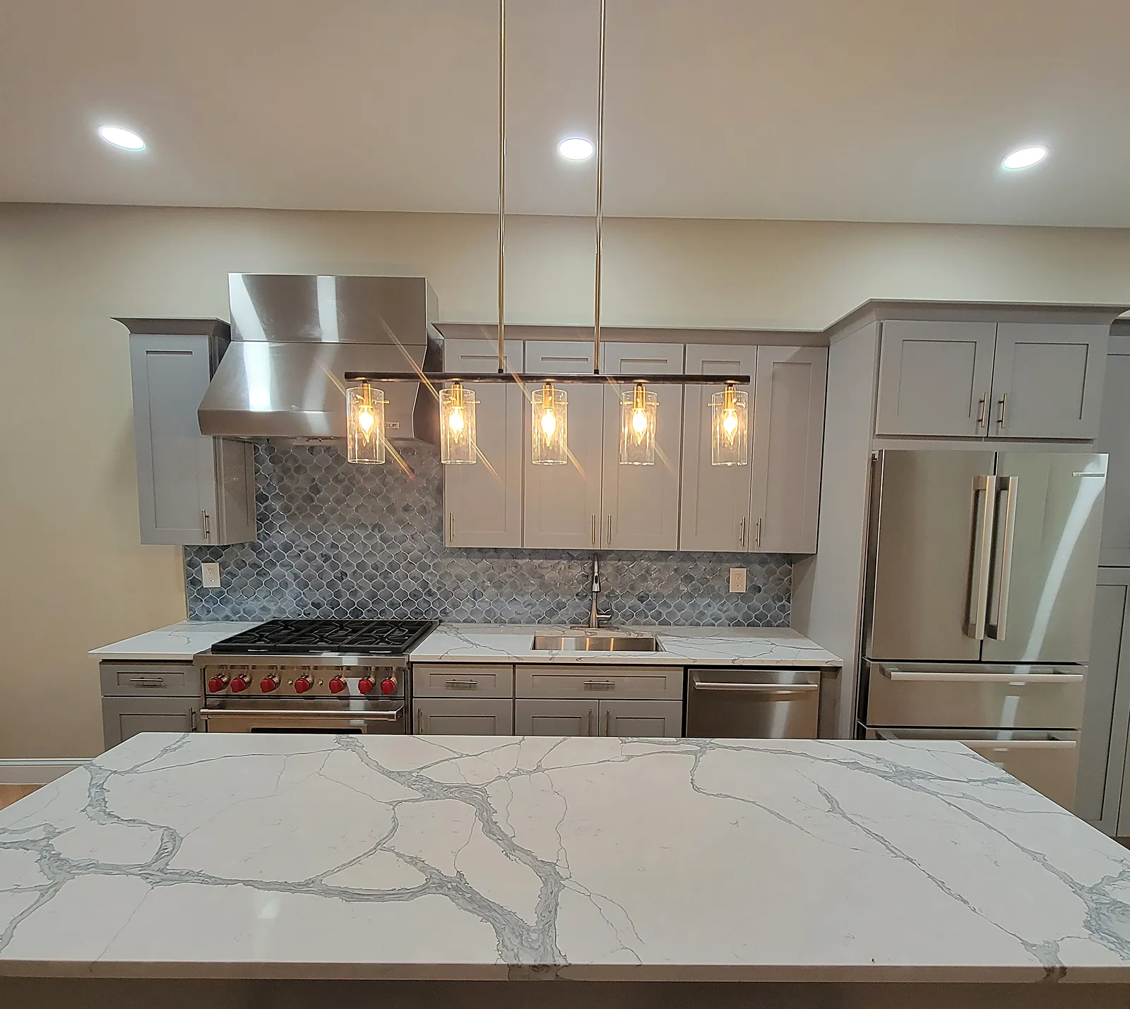 Kitchen remodel in the Bronx, NY: a marble-look island in front of gray shaker cabinets, a blue mosaic backsplash and a five-light pendant