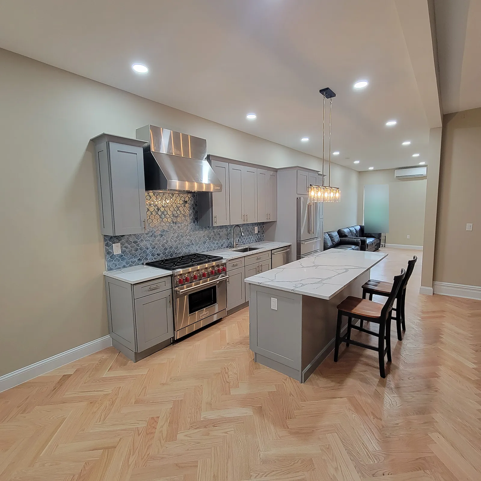 Kitchen remodel in the Bronx, NY: gray shaker cabinets and a marble-look island on a herringbone wood floor that runs into the living area