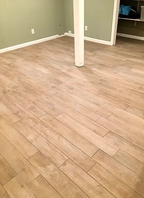 Basement remodel in Commack, NY: a wood-look plank tile floor laid on an angle in a sage-green basement room