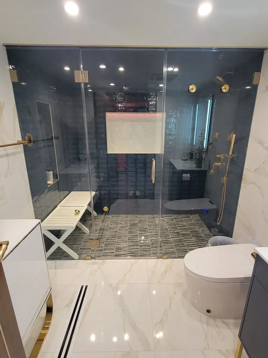 Bathroom remodel in Dix Hills, NY: glass-enclosed walk-in shower tiled in blue, with gold fixtures and a bench