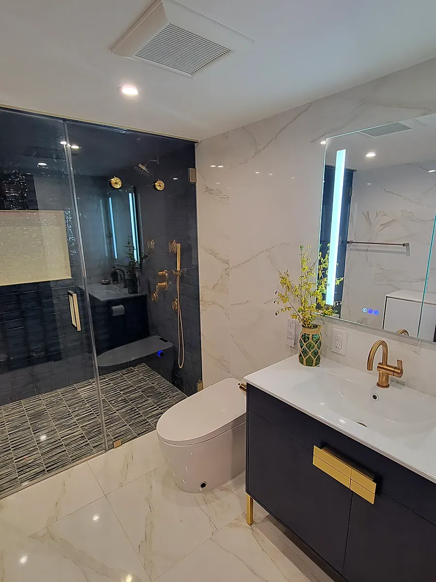 Bathroom remodel in Dix Hills, NY: a navy vanity with gold pulls beside a glass shower with dark blue tile and a white marble-look floor
