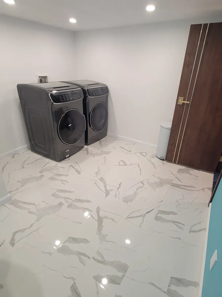 Laundry room remodel in Dix Hills, NY: marble-look tile floor, white walls and recessed lights, with washer and dryer