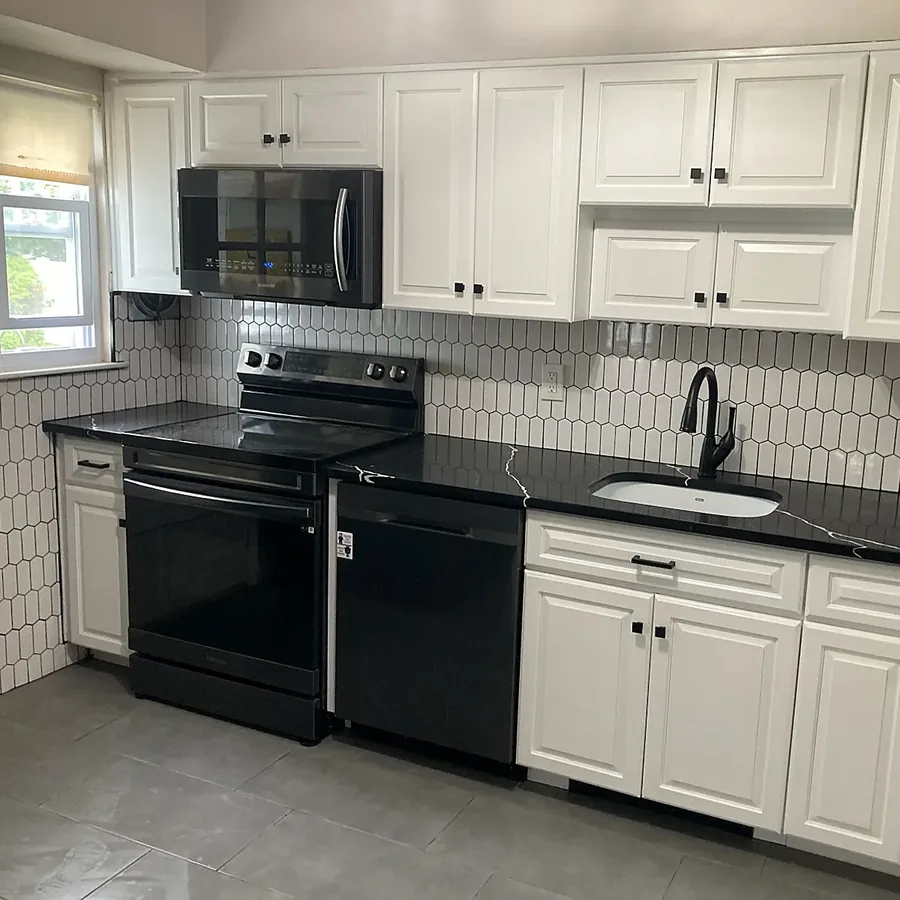 Kitchen remodel in East Northport, NY: a wall of white cabinets with a black range, black counters and a white elongated hexagon backsplash