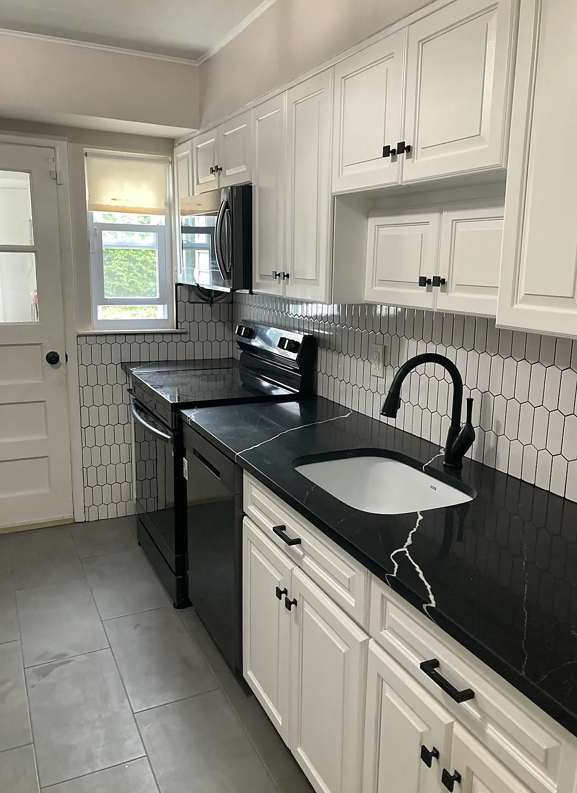 Kitchen remodel in East Northport, NY: white raised-panel cabinets with black hardware, a black marble-look counter and white picket backsplash