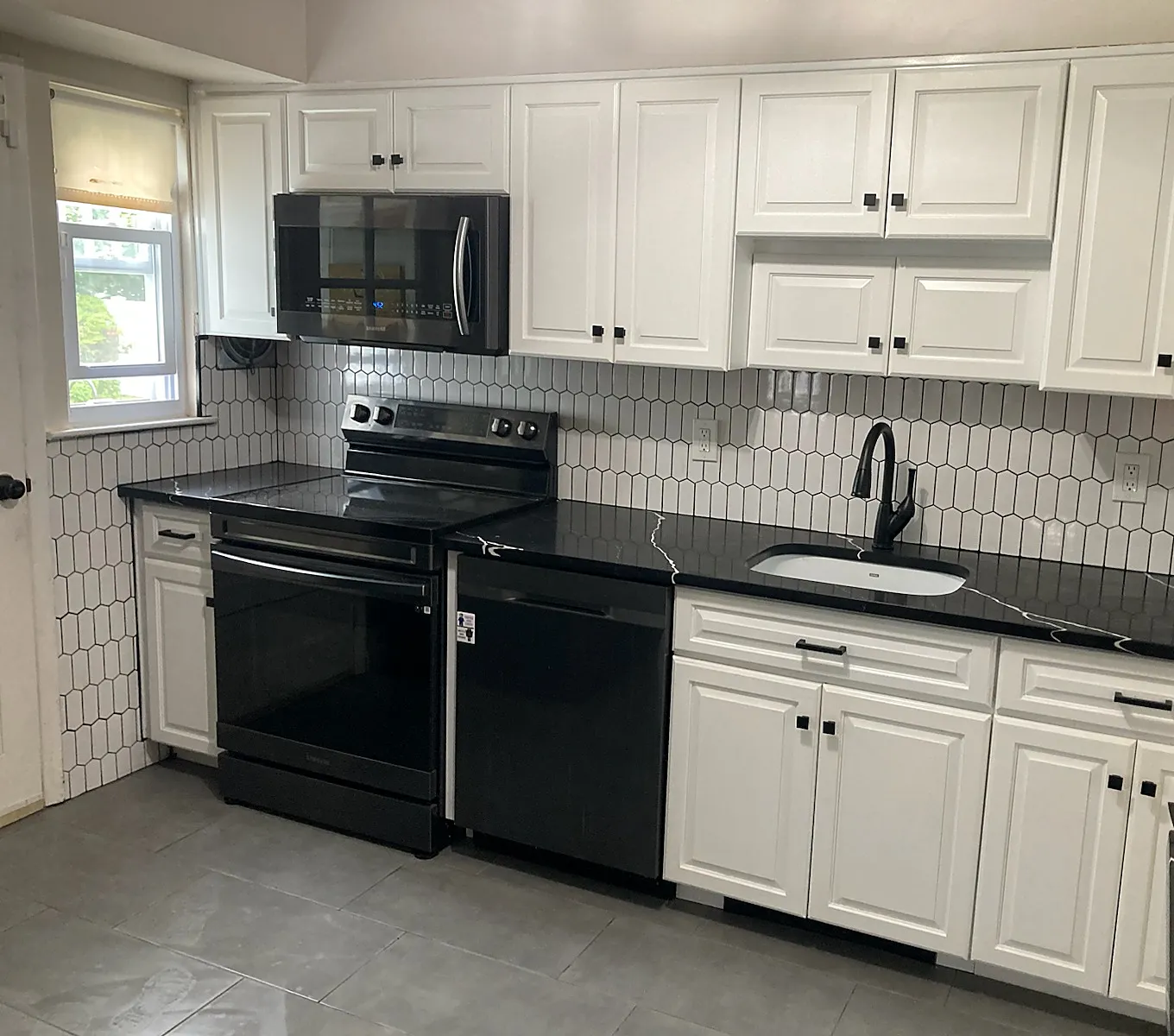Kitchen remodel in East Northport, NY: a wall of white cabinets with a black range, black counters and a white elongated hexagon backsplash