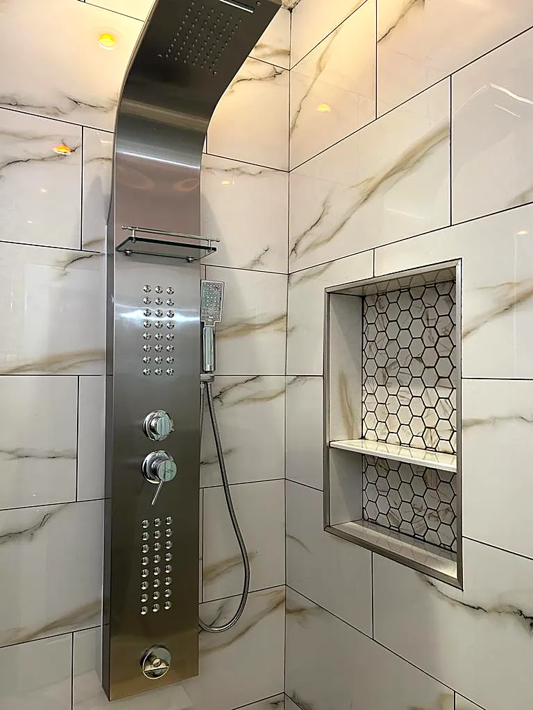 Shower remodel in Flushing, Queens, NY: a stainless shower panel and a hexagon mosaic niche in white and gold marble-look tile