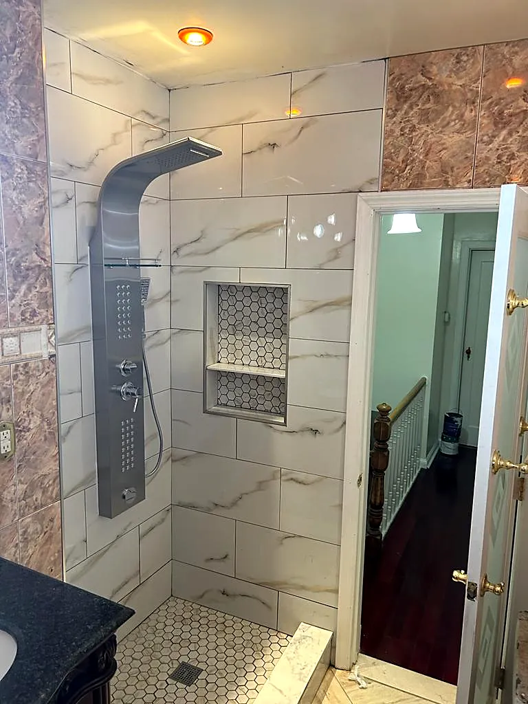 Bathroom remodel in Flushing, Queens, NY: a walk-in shower with marble-look wall tile, a stainless shower panel, mosaic niche and hexagon floor