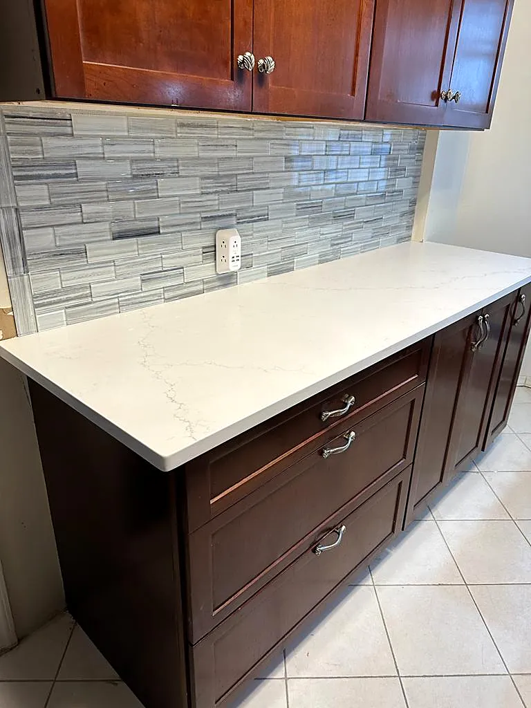 Kitchen remodel in Flushing, Queens, NY: a run of cherry drawer cabinets with a long white counter and a gray glass tile backsplash