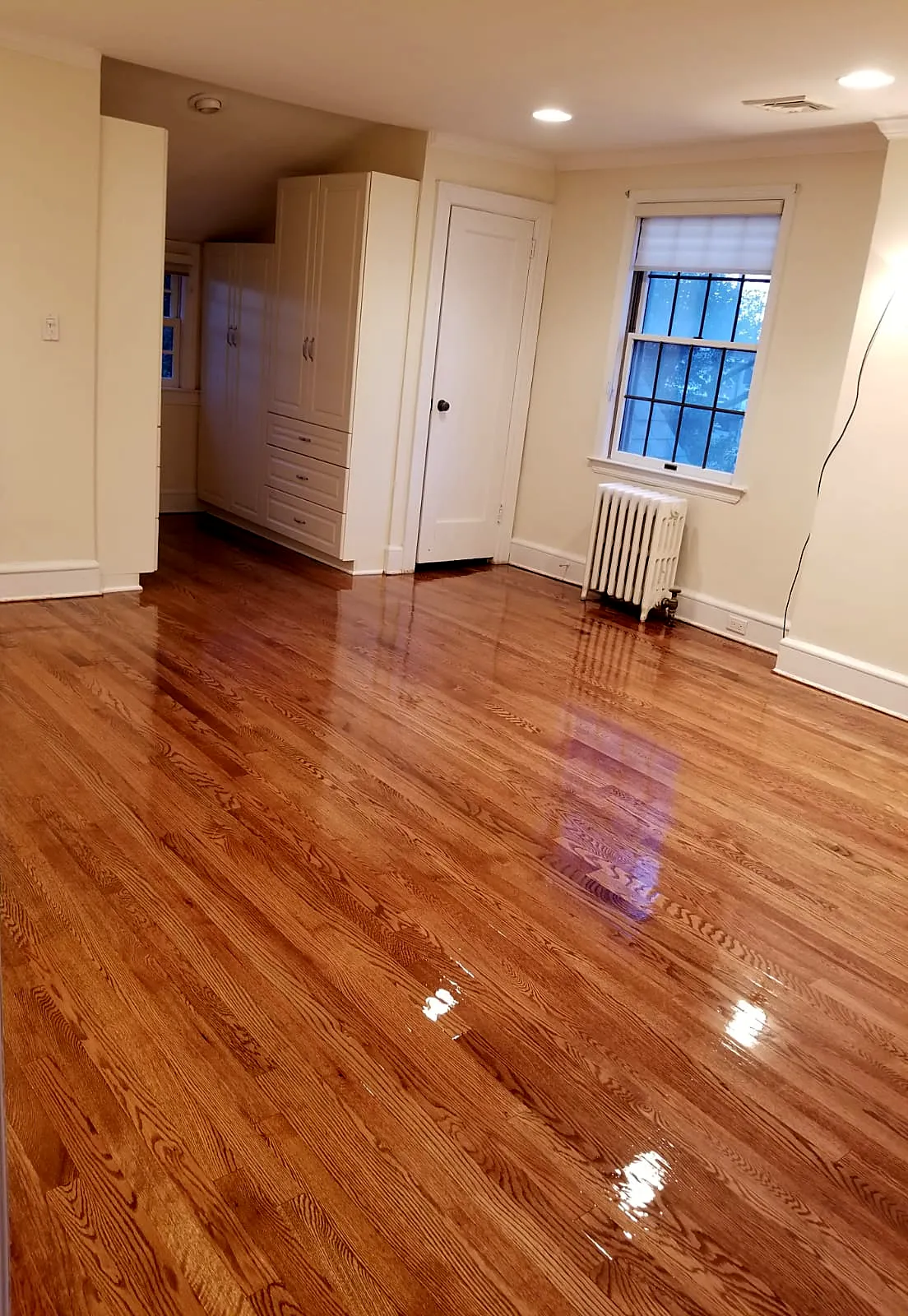 Bedroom remodel in Garden City, NY: a refinished glossy honey wood floor in a bedroom with white built-in closets and a radiator