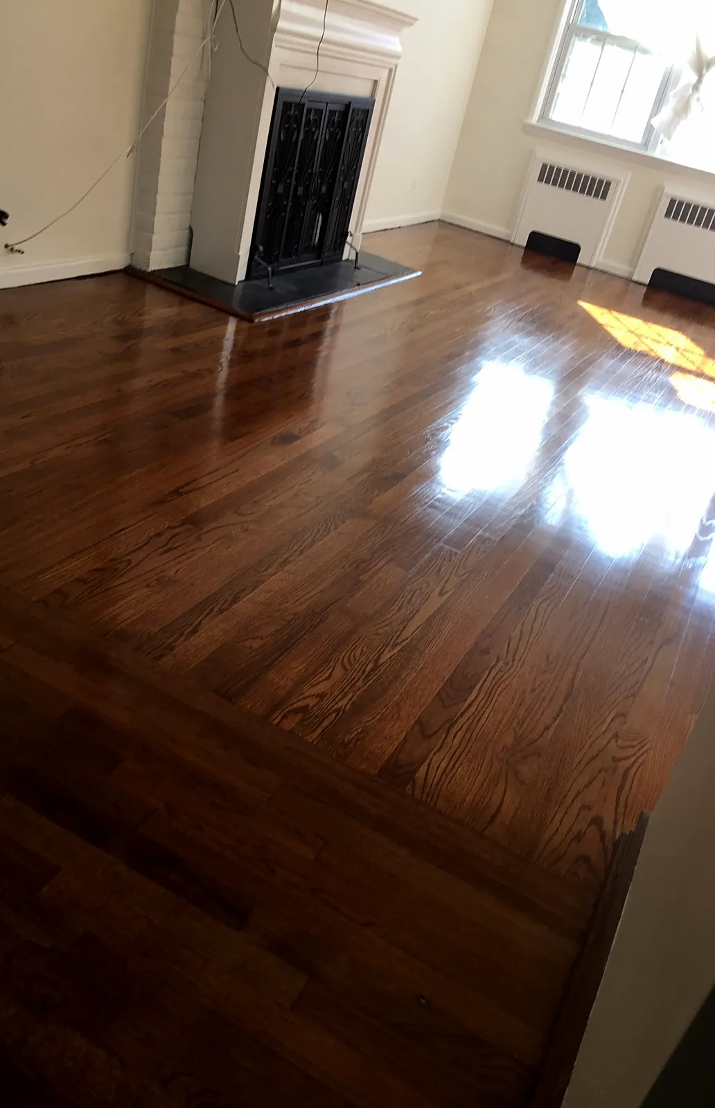 Living room remodel in Garden City, NY: a refinished deep brown wood floor with a high gloss in a living room with a white brick fireplace