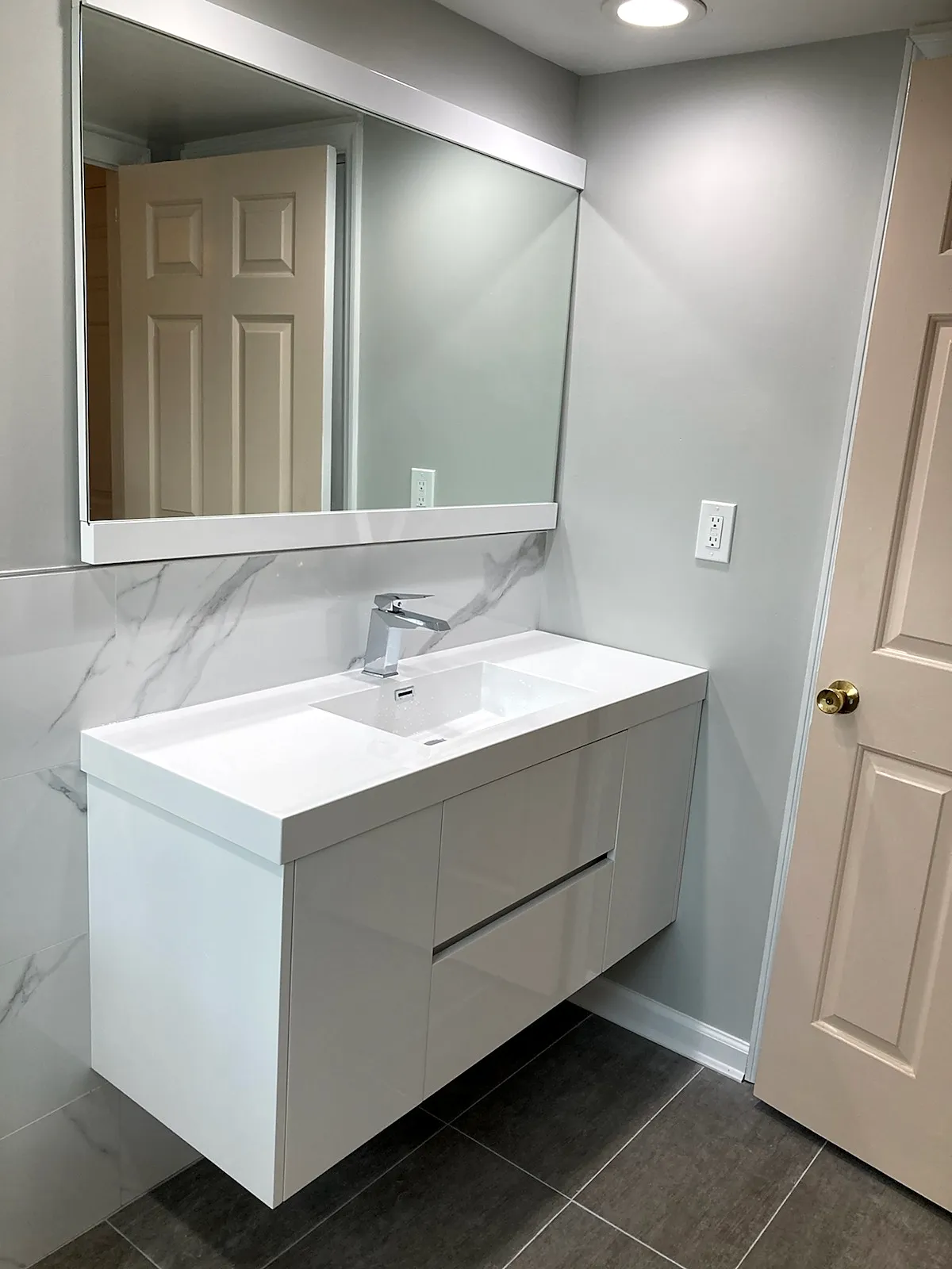 Bathroom remodel in Glen Head, NY: a white floating vanity with a wide mirror, a marble-look backsplash and gray floor tile
