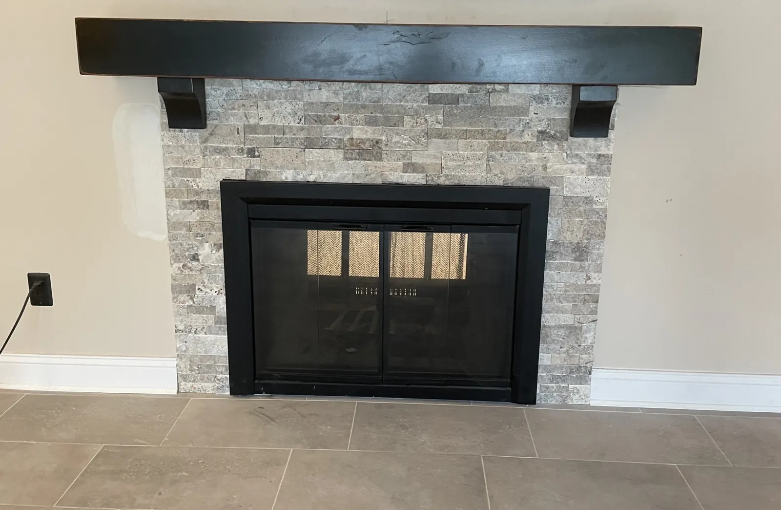 Fireplace remodel in Levittown, NY: stacked-stone fireplace surround with a dark wood mantel and black doors