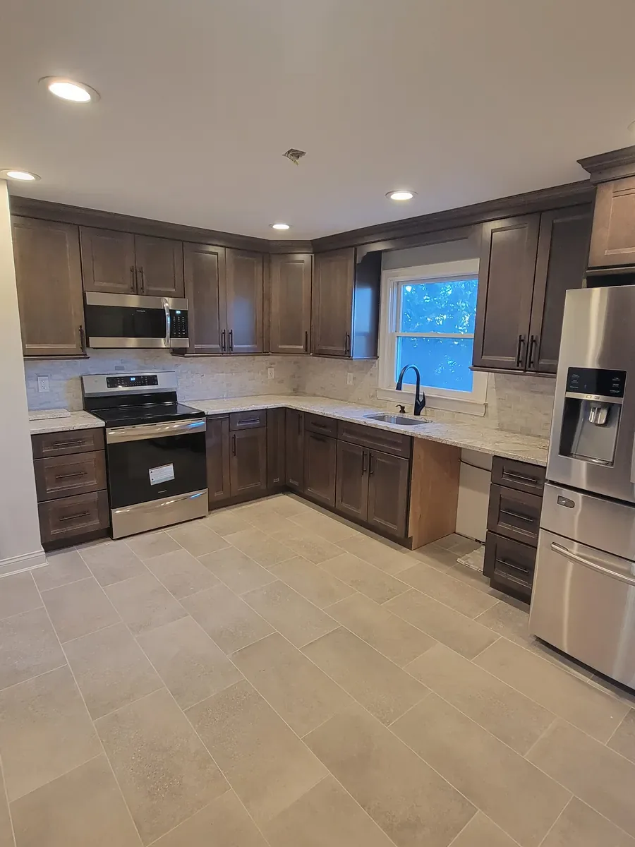 Kitchen remodel in Levittown, NY: L-shaped kitchen with dark wood cabinets, light counters, stainless appliances and tile floor
