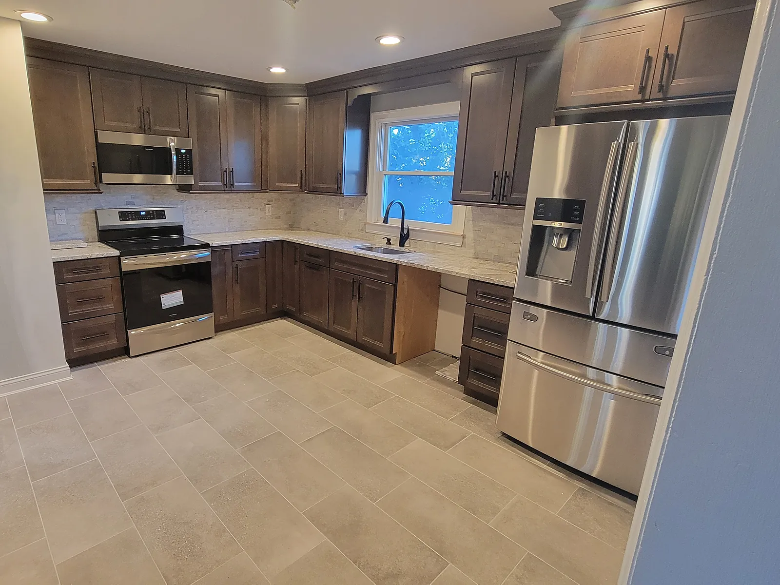 Kitchen remodel in Levittown, NY: dark wood cabinets, light speckled counters and a large gray tile floor