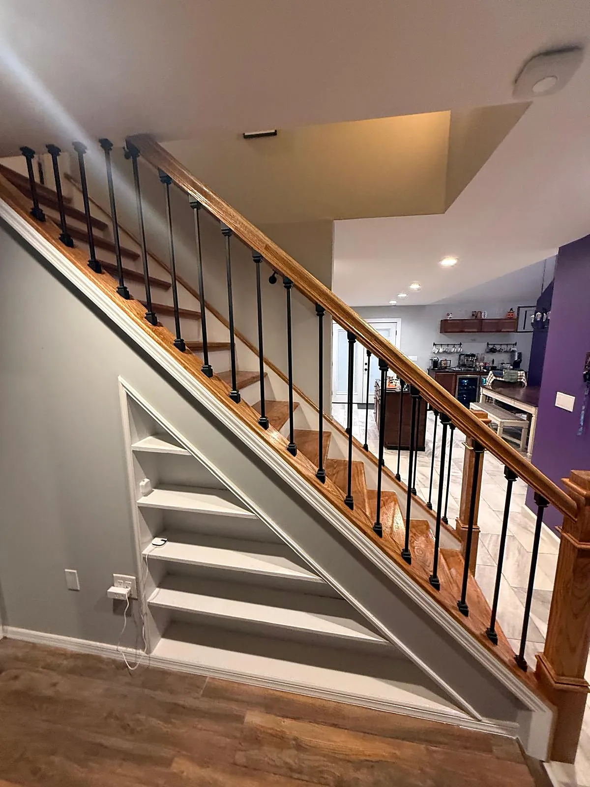 Staircase remodel in Levittown, NY: wood stairs with a wood handrail and black metal spindles, with built-in white shelves under the stairs