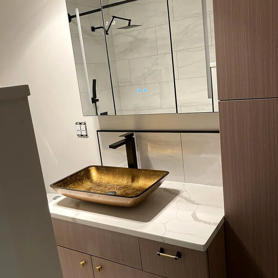 Bathroom remodel in Lindenhurst, NY: a wood-look vanity with a gold glass vessel sink, a lighted mirror cabinet and a tall linen cabinet