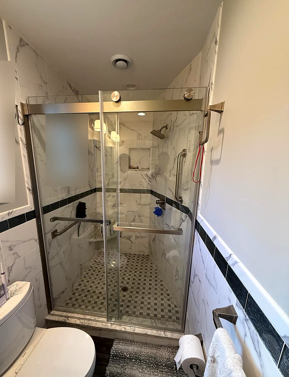 Bathroom remodel in Malverne, NY: a glass-door shower with white marble-look tile, a dark accent stripe and a mosaic shower floor