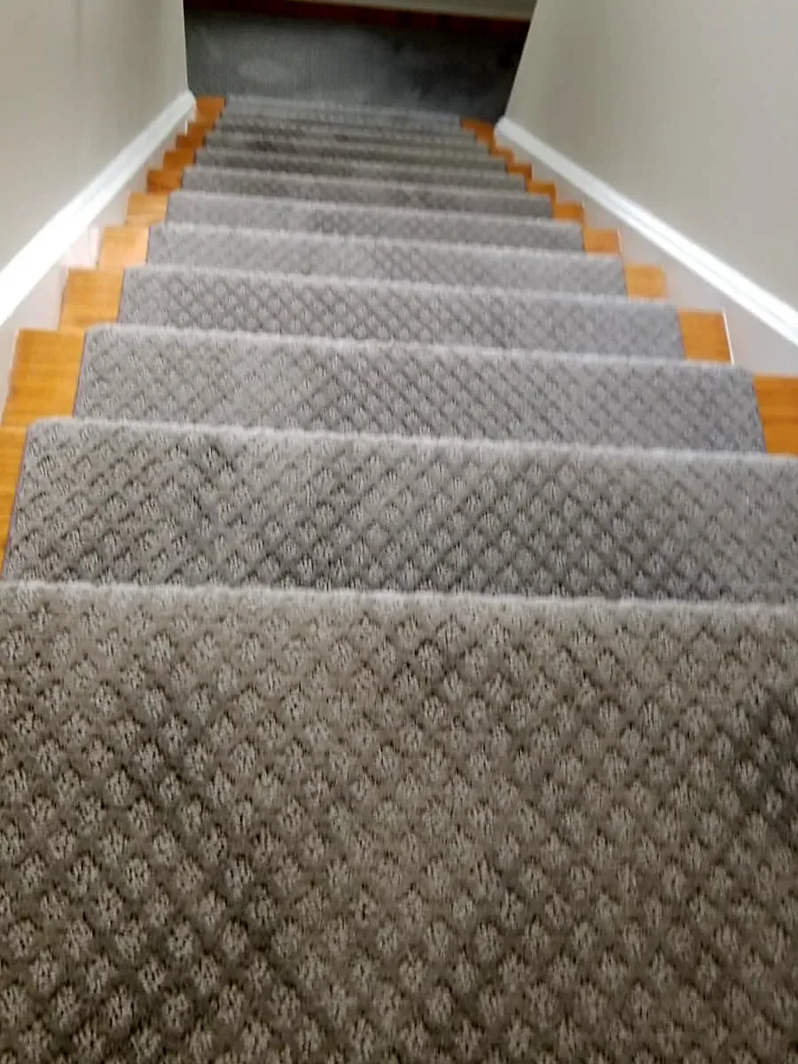 Staircase remodel in Manhasset, NY: a gray diamond-pattern stair runner over natural wood treads leading up to a bright landing