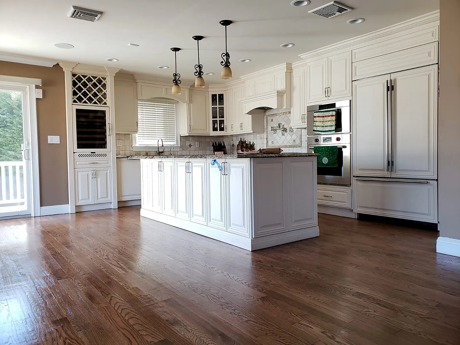 Kitchen remodel in Massapequa Park, NY: a refinished medium-brown wood floor running through an open white kitchen with a center island