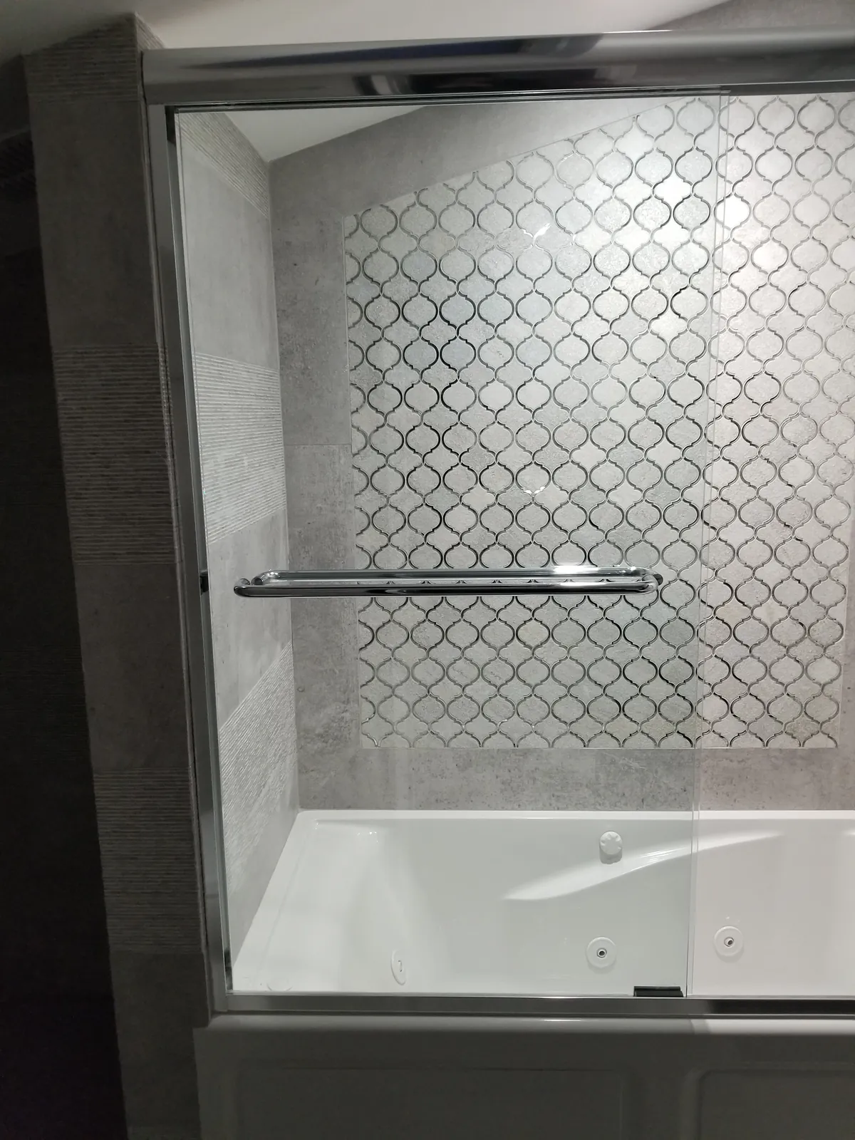 Bathroom remodel in Massapequa, NY: jetted tub with a sliding glass door in front of an arabesque mosaic wall