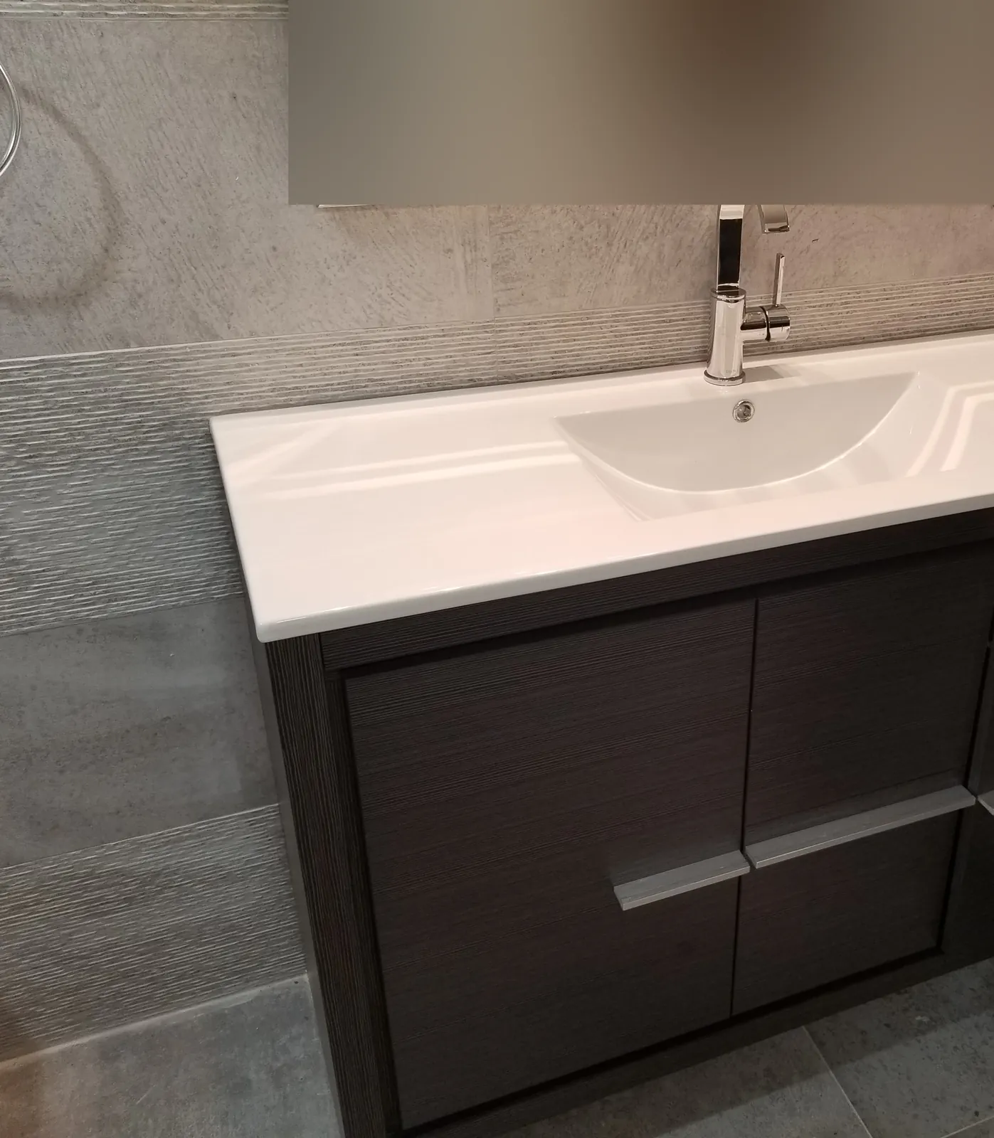 Bathroom remodel in Massapequa, NY: dark wood-grain vanity with a white integrated sink and textured gray wall tile