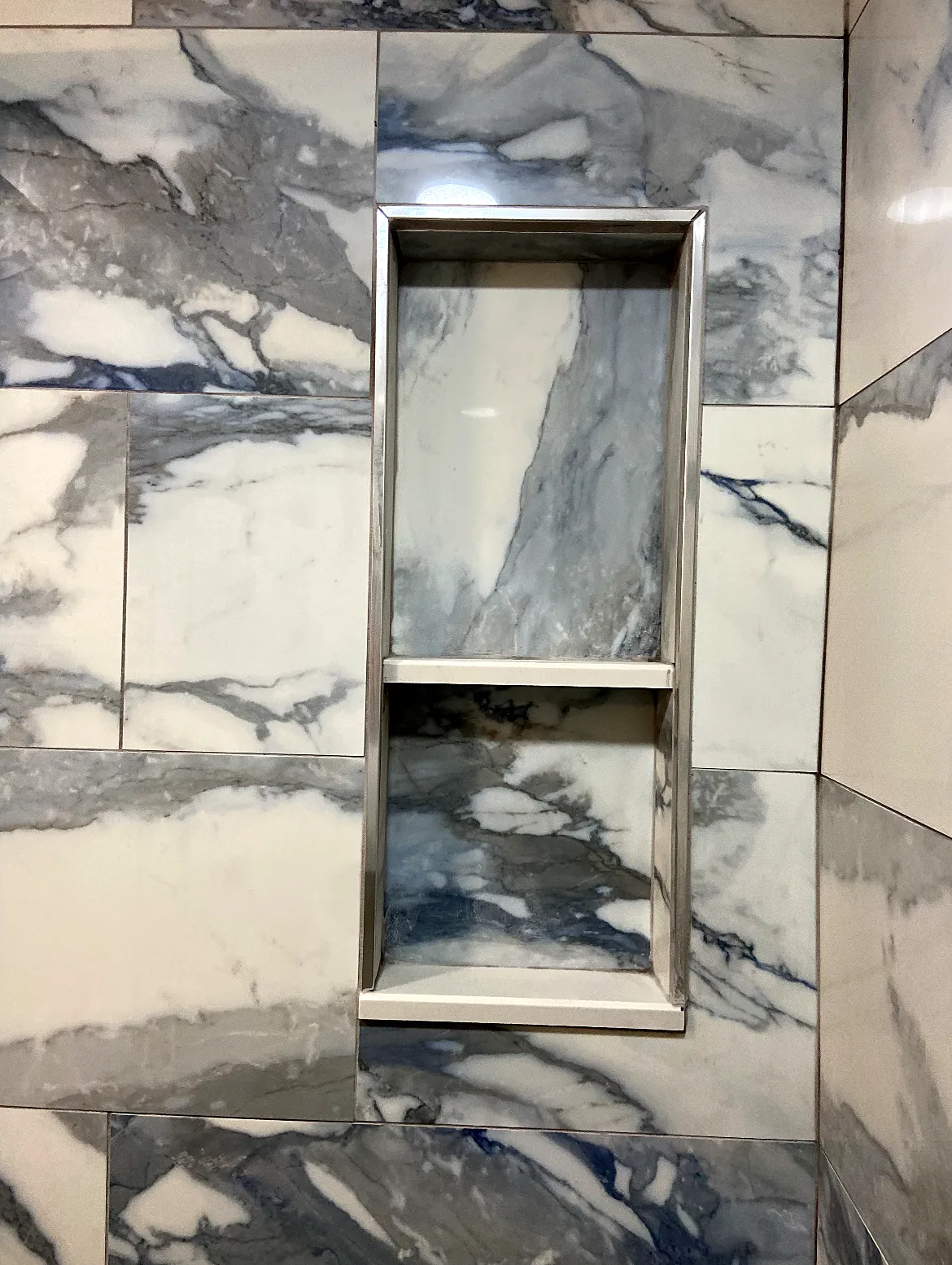 Shower remodel in Medford, NY: a recessed shower niche with a metal trim set in blue-gray marble-look wall tile