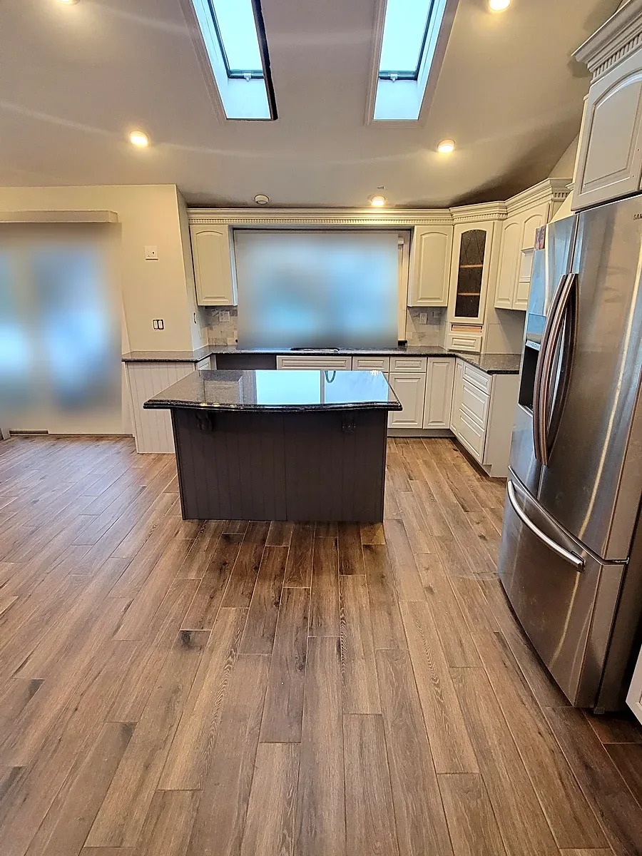 Kitchen remodel in Merrick, NY: vaulted ceiling with skylights over a gray island and a wood-look plank floor