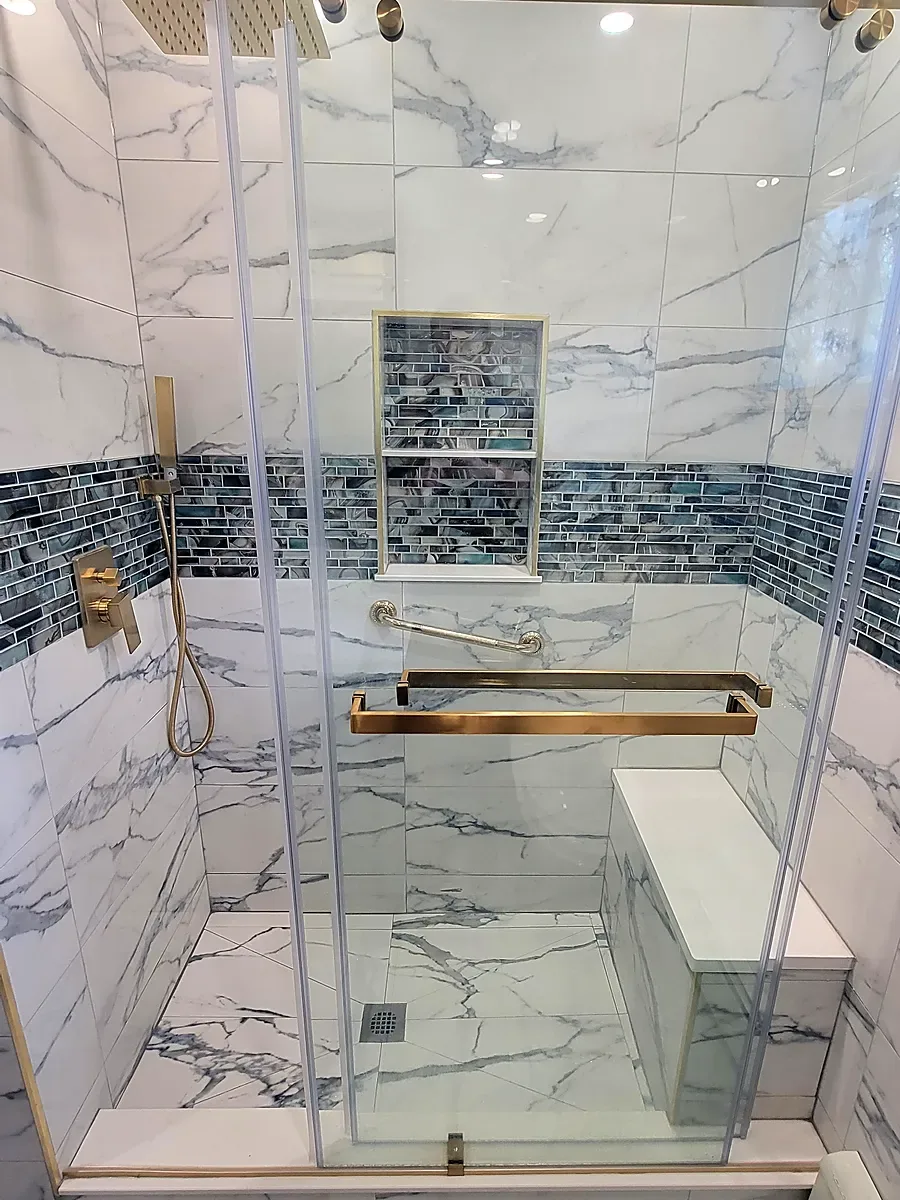 Shower remodel in Middle Island, NY: a glass sliding-door shower with a bench, gold fixtures, a mosaic niche and marble-look tile