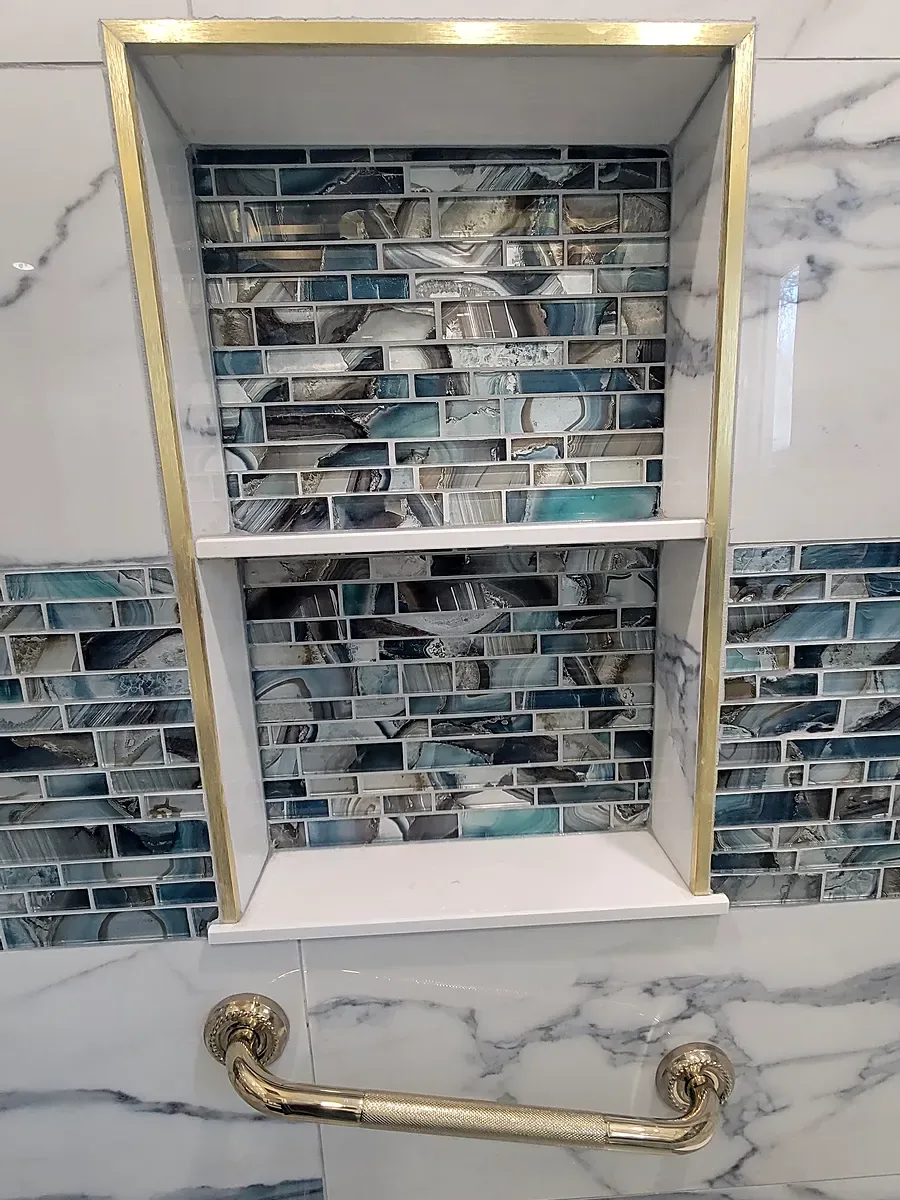 Shower niche remodel in Middle Island, NY: a gold-trimmed shower niche lined with blue glass tile above a brass grab bar