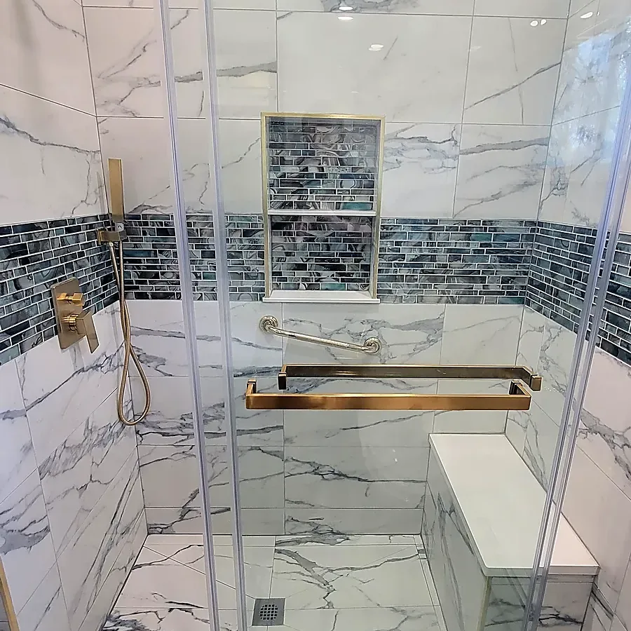 Shower remodel in Middle Island, NY: a glass sliding-door shower with a bench, gold fixtures, a mosaic niche and marble-look tile