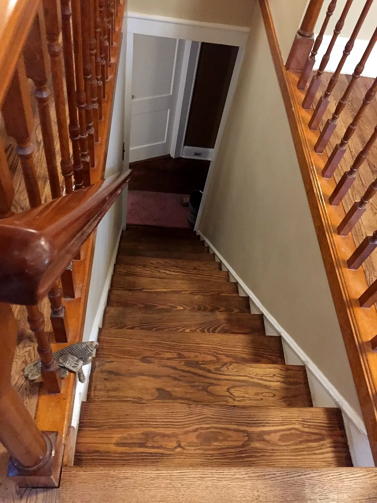 Staircase remodel in Mineola, NY: refinished honey-brown wood stair treads between a turned-spindle railing and a white-trimmed wall