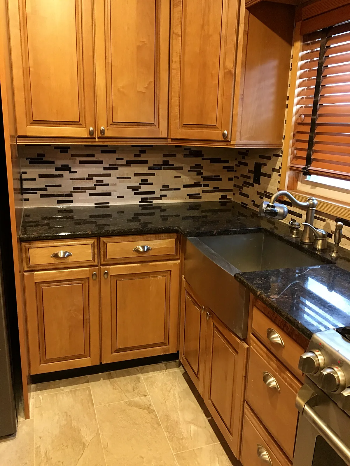 Kitchen remodel in New Hyde Park, NY: wood cabinets with a dark stone-look counter, a farmhouse sink and a brown and cream linear tile backsplash