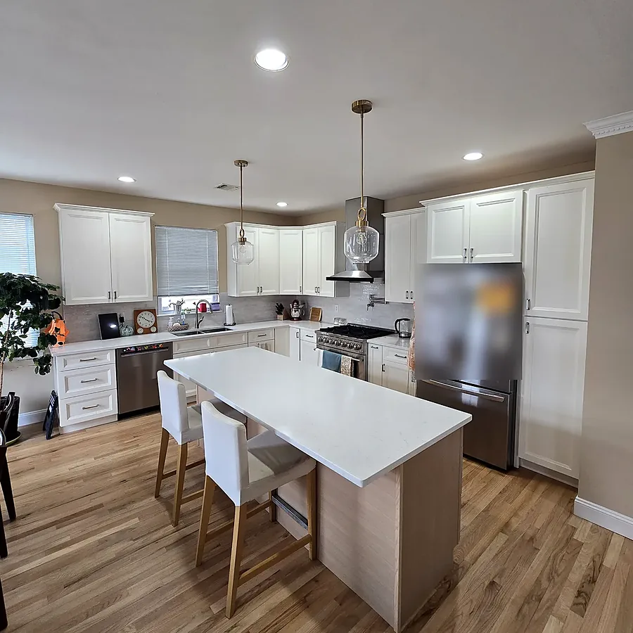 Kitchen remodel in North Bellmore, NY: white shaker cabinets, a light wood island with a white top, brass pendant lights and a wood floor
