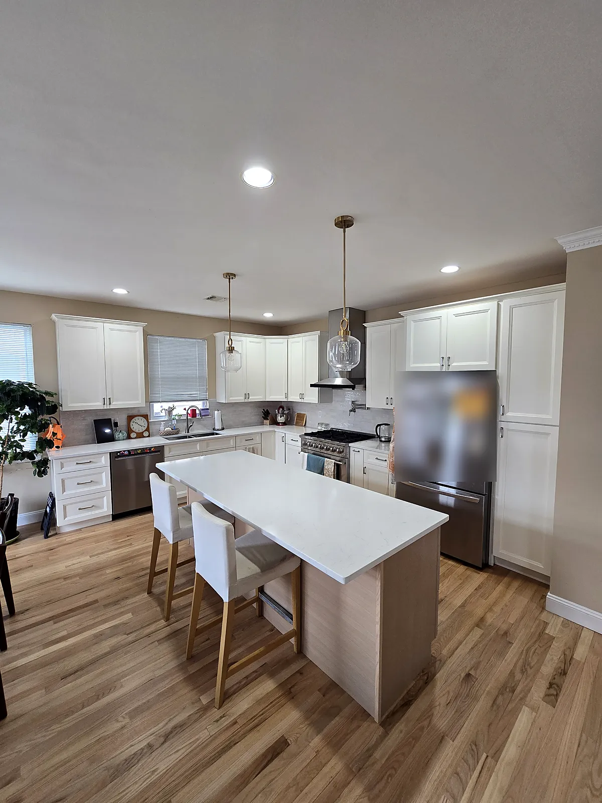 Kitchen remodel in North Bellmore, NY: white shaker cabinets, a light wood island with a white top, brass pendant lights and a wood floor