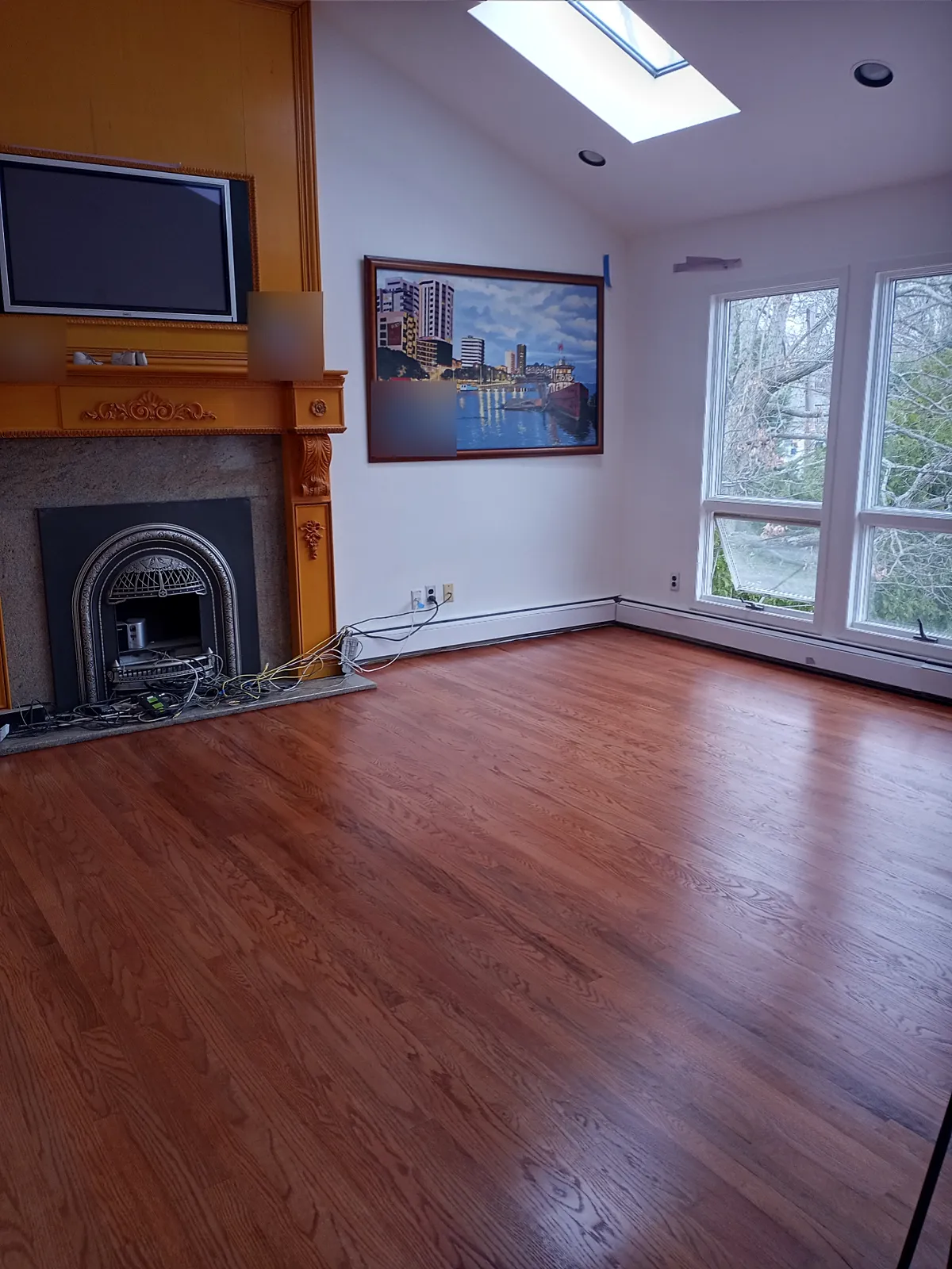 Living room remodel in North Bellmore, NY: a refinished reddish-brown wood floor in a vaulted living room with a skylight and a fireplace