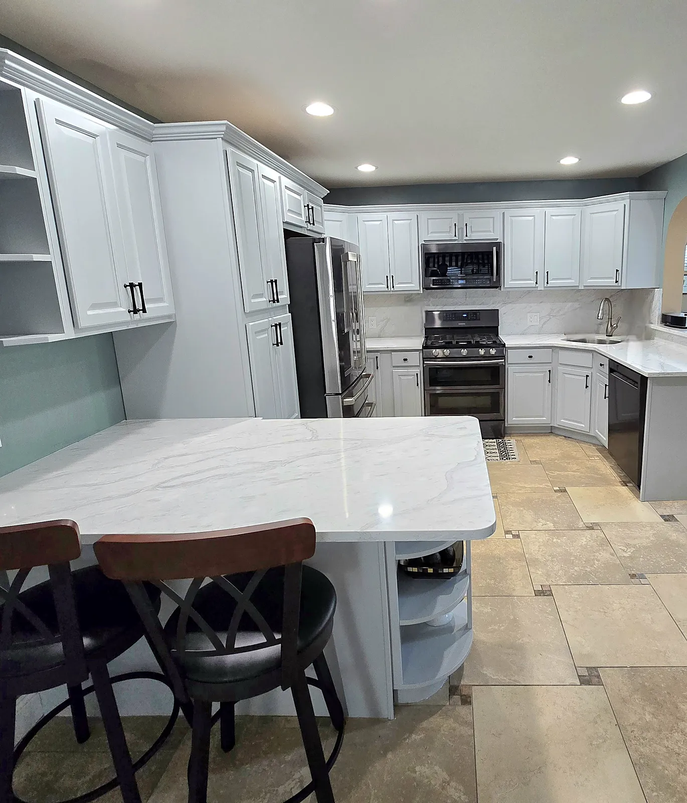 Kitchen remodel in North Merrick, NY: white cabinets with black pulls, a white marble-look peninsula and backsplash, and a stainless range