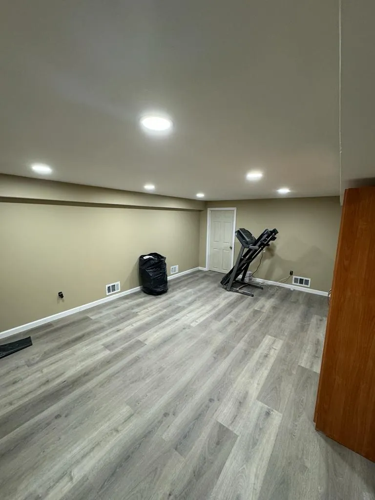 Basement remodel in Oceanside, NY: gray vinyl plank floor, beige walls and recessed lights