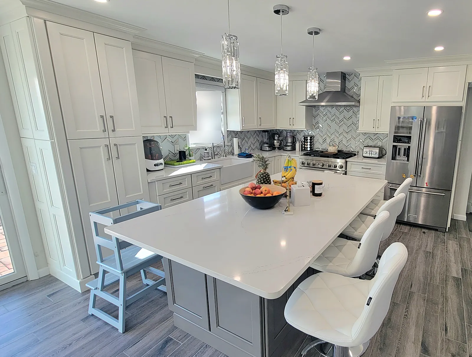 Kitchen remodel in Oceanside, NY: white shaker cabinets, a large white island with gray base, a chevron mosaic backsplash and crystal pendants