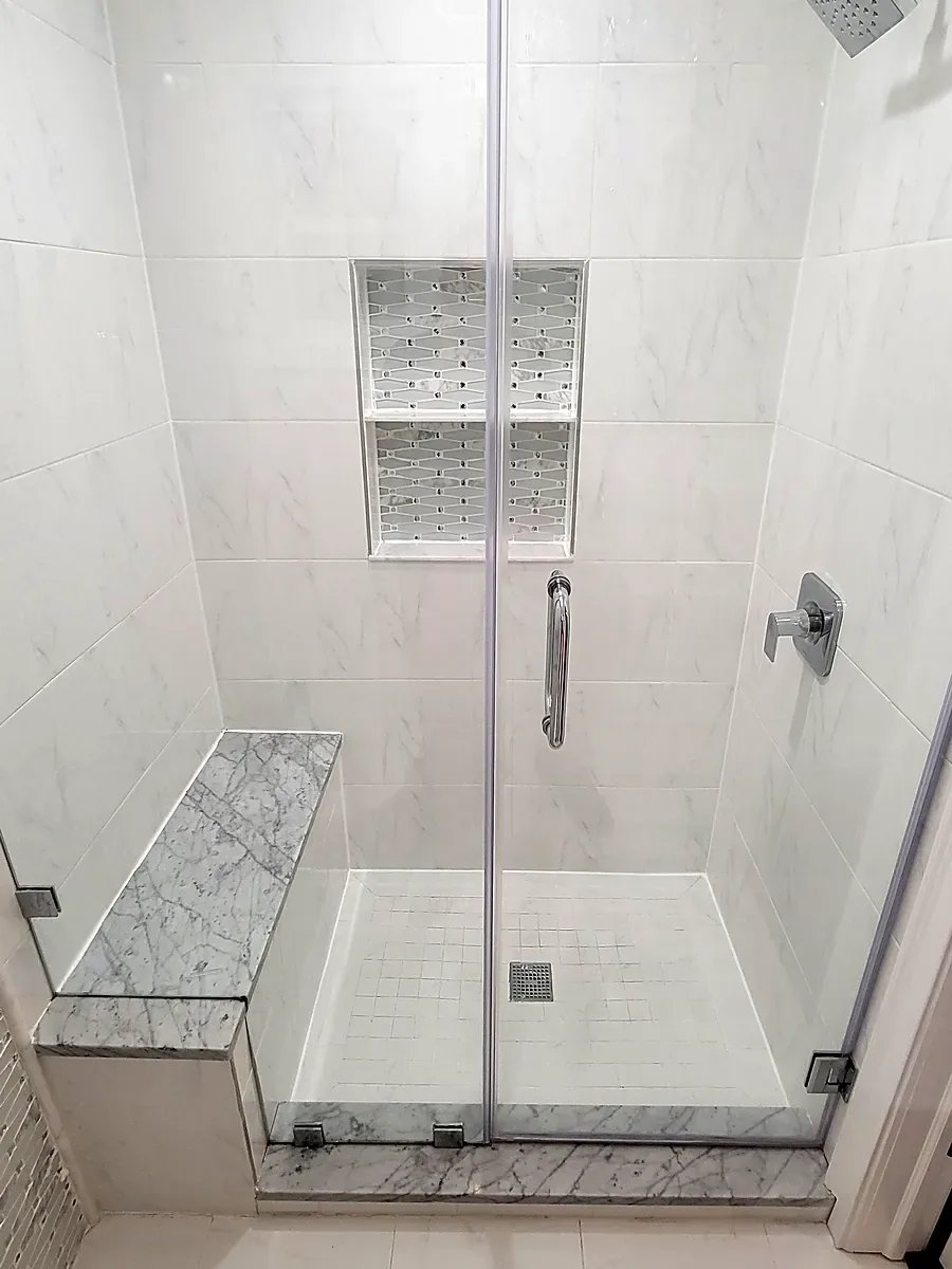 Bathroom remodel in Plainview, NY: walk-in glass shower with a marble bench and two tiled niches