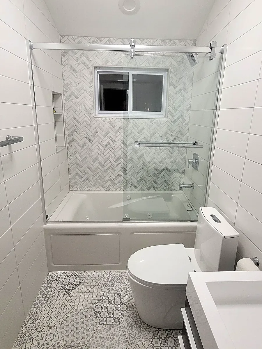 Bathroom remodel in Plainview, NY: tub with a sliding glass door, herringbone marble-look tile, a niche and a patterned hexagon floor