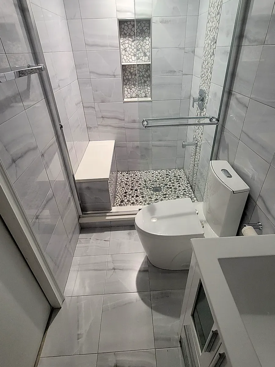 Bathroom remodel in Plainview, NY: large marble-look floor tile, white vanity and a shower with a bench and niches