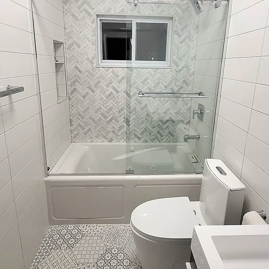 Bathroom remodel in Plainview, NY: tub with a sliding glass door, herringbone marble-look tile, a niche and a patterned hexagon floor