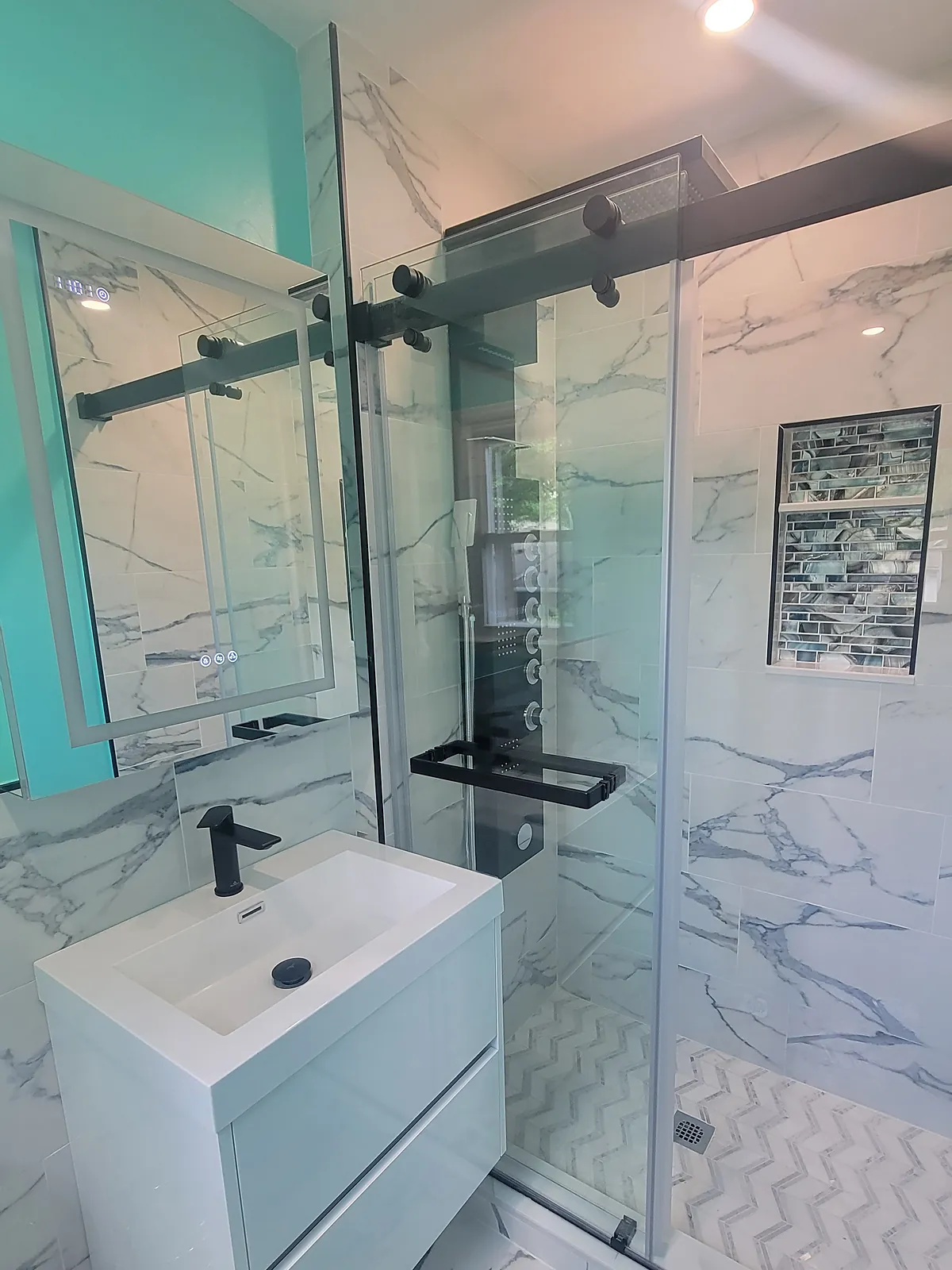Bathroom remodel in Port Washington, NY: a glass shower with marble-look tile, a white floating vanity and black fixtures