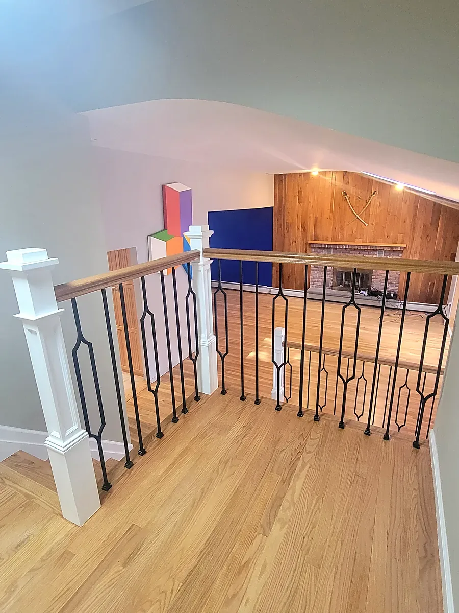 Living room remodel in Port Washington, NY: a black metal spindle railing with a white post overlooking a lower room with a refinished wood floor