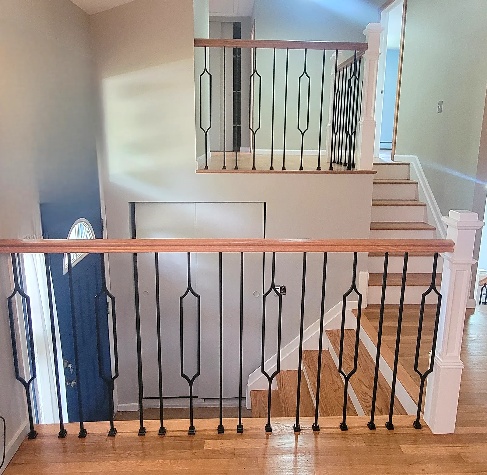 Staircase remodel in Port Washington, NY: split-level stairs with wood handrails, white newel posts and black metal spindles with a diamond pattern